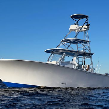 White center-console sport fishing boat with a T-top and tower underway on open blue water.