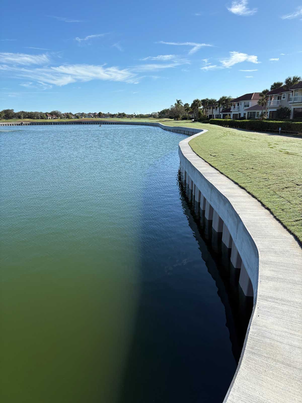 Newly built concrete seawall lining a retention pond beside a golf course and townhomes, with no business or town identifiable in the photo.
