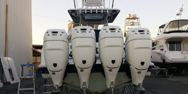 Four-outboard center-console boat stern at a boat service yard with a cruiser parked beside it.