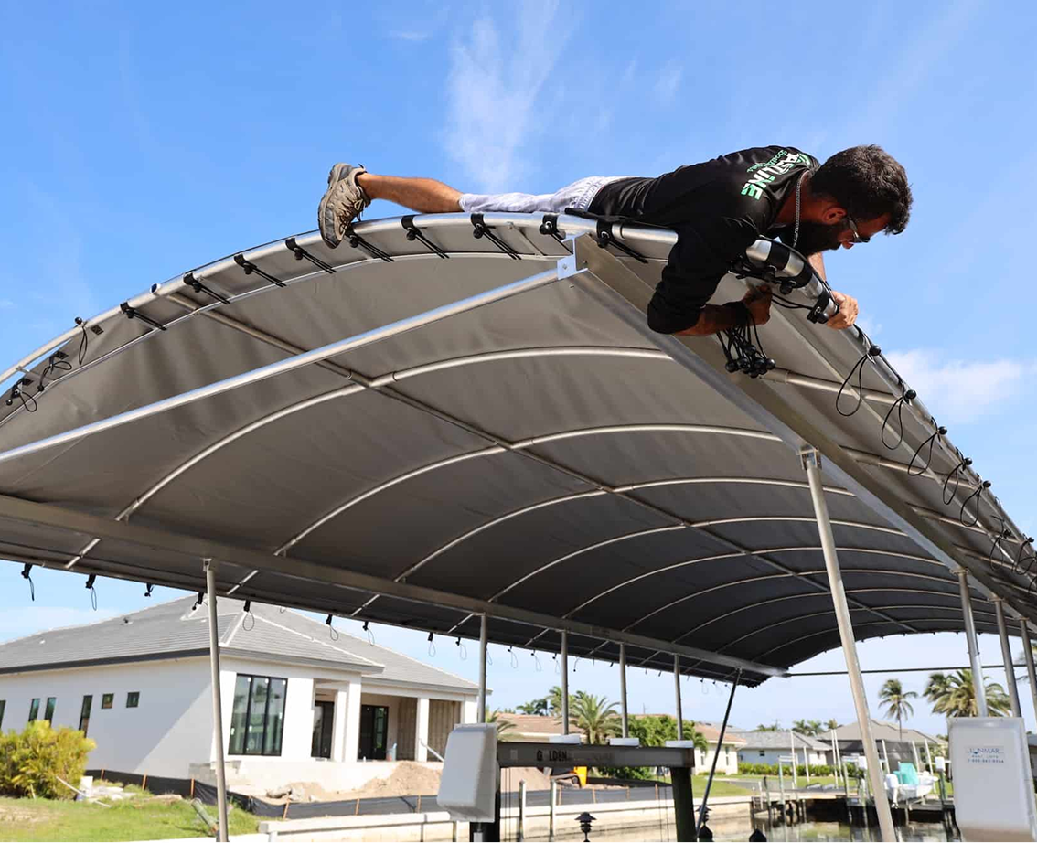 Technician installing a canvas canopy cover on a boat lift at a waterfront property, Cape Coral area.