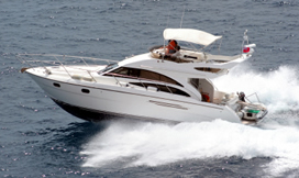 White motor yacht with a flybridge and hardtop cruising fast across blue water, leaving a white wake.