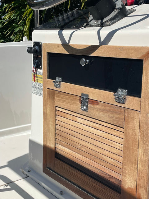 Teak-framed storage locker with louvered door and stainless steel latches on a white boat deck.