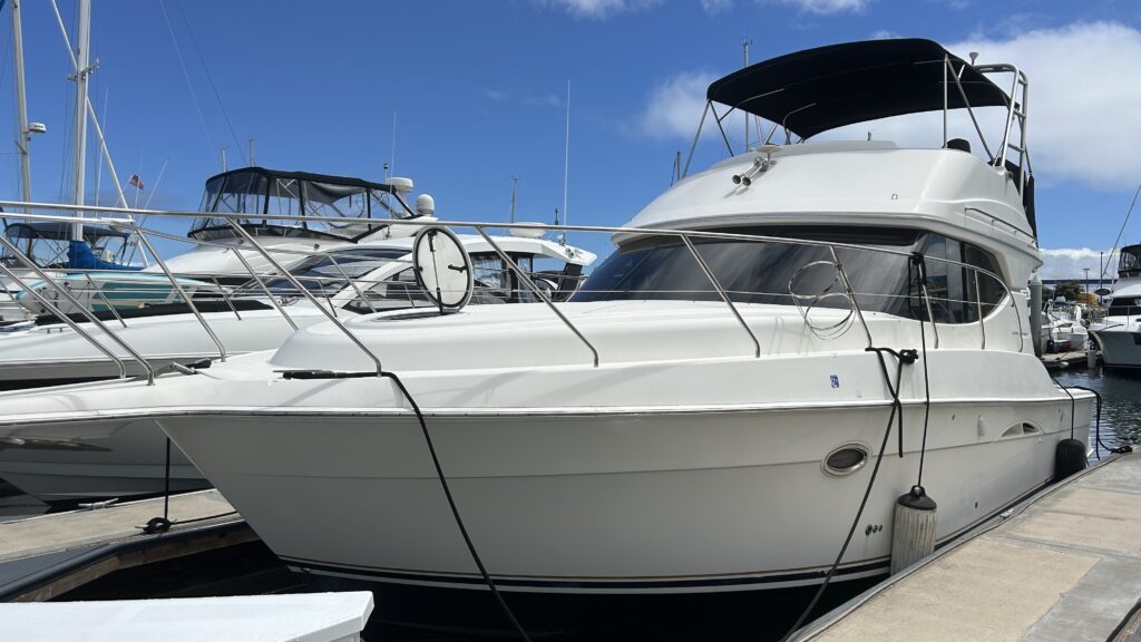 White motor yacht moored at a marina dock with neighboring boats, photographed on a sunny day.
