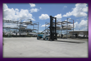 Forklift beside multi-level dry-stack boat storage racks in an outdoor yard.