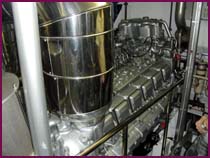Marine diesel engine with a polished stainless steel exhaust riser in an engine compartment.