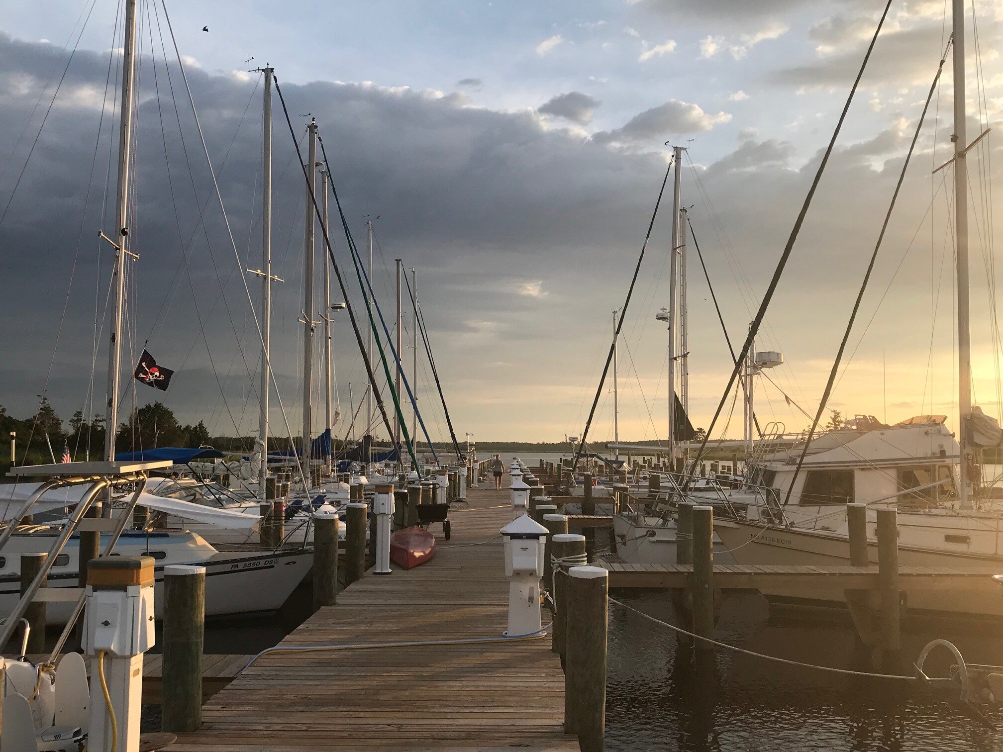 Sailboats moored along a wooden dock at sunset at a marina, with pedestal power posts and a red kayak on the pier.