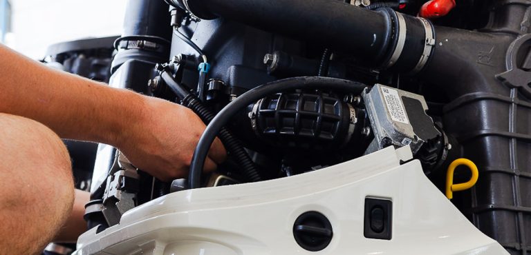 Technician servicing a marine outboard engine with fuel lines and wiring exposed on a white cowling.
