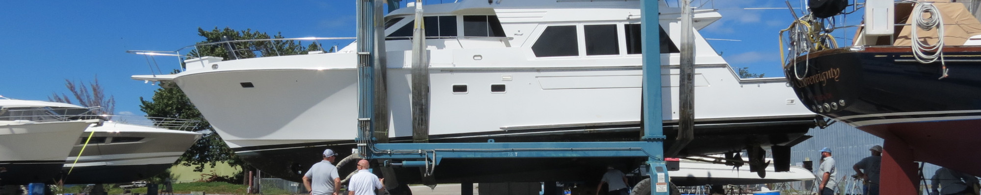 White motor yacht being hauled out on a travel lift with workers guiding it at a boatyard.