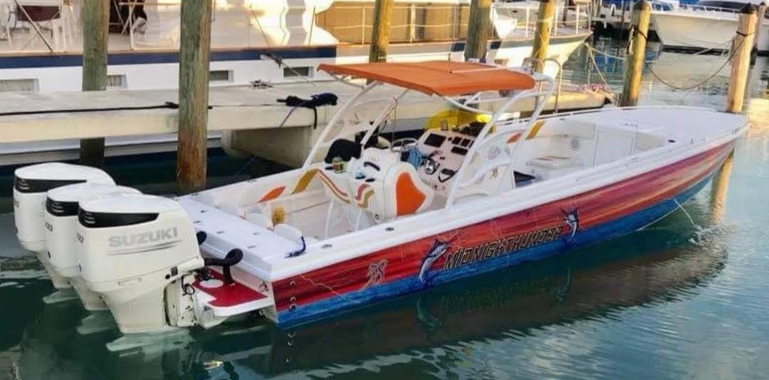 Center console sportfishing boat Midnight Thunder with triple Suzuki outboard motors tied up at a marina dock.