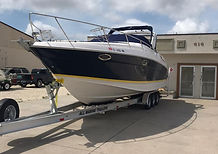 Navy and white cabin cruiser on a dual-axle trailer in front of a dealer building with the number 418 on it.