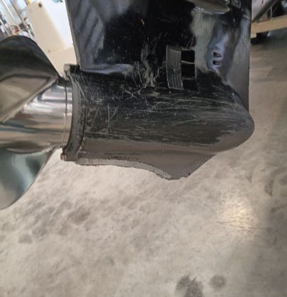 Scraped and damaged outboard motor gearcase with a stainless steel propeller on a shop floor.