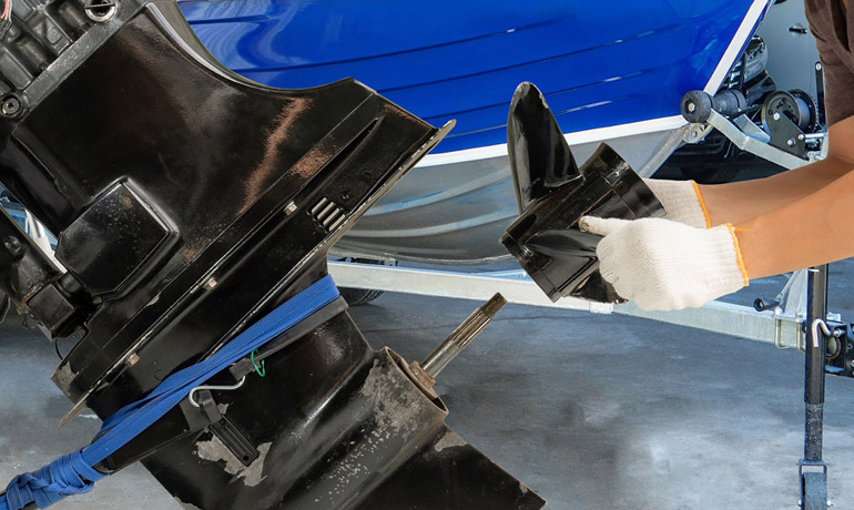 Outboard motor lower unit and propeller being serviced on a boat trailer in a workshop.
