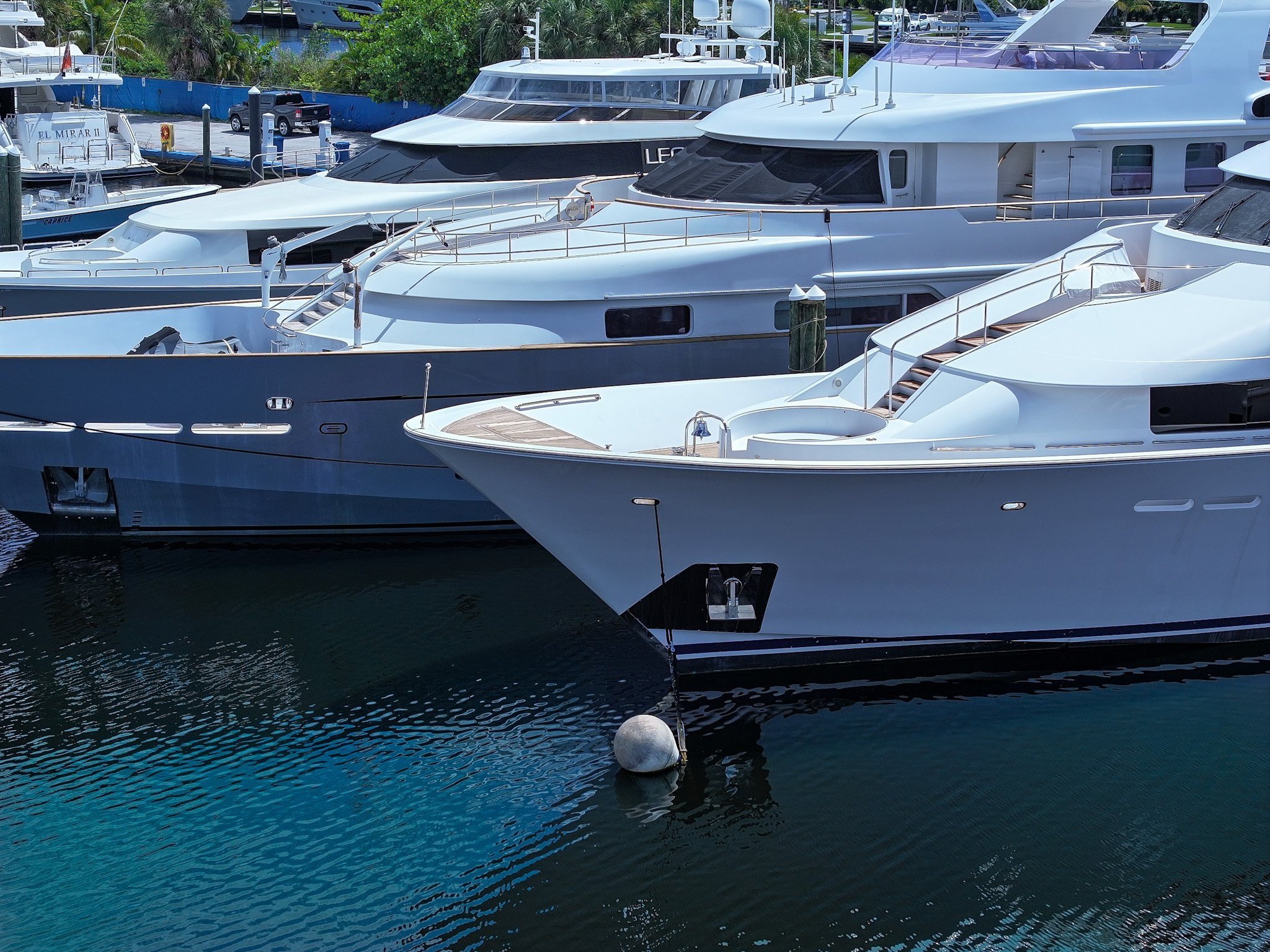 Large white motor yachts moored in a marina, including one named El Mirar II nearby, with a bow anchor and mooring buoy in the foreground.