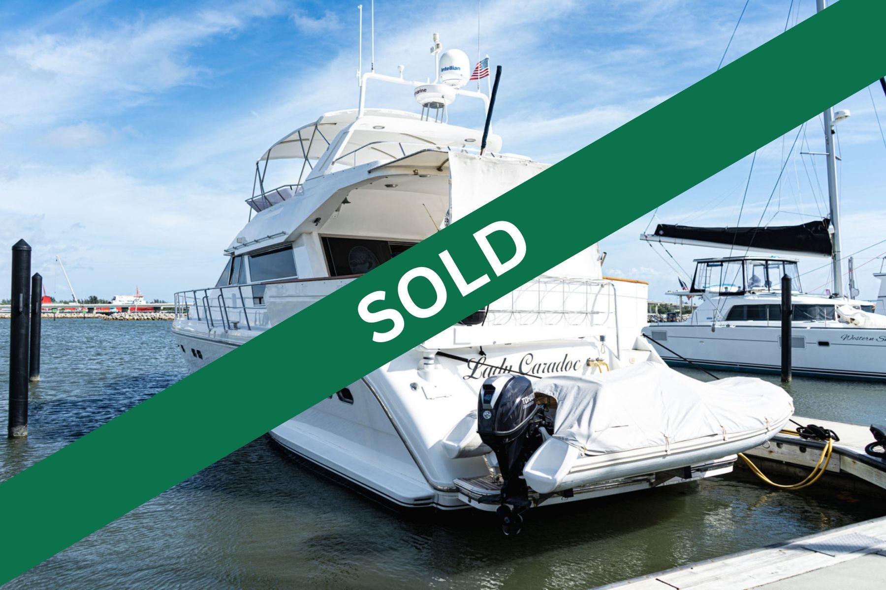 Motor yacht Lady Caradoc with a covered tender and outboard motor docked at a marina, with a catamaran named Western Star moored beside it.