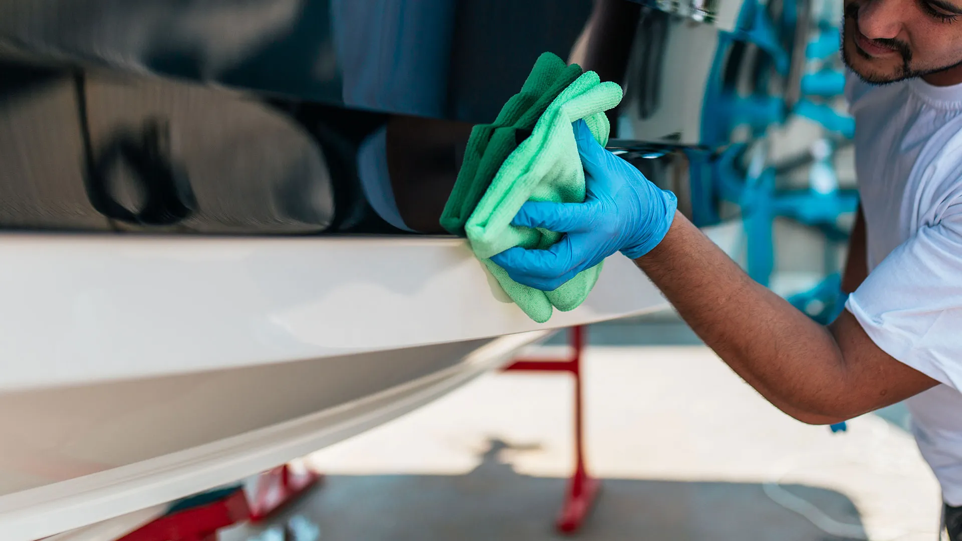 Technician in blue gloves wiping down the white hull of a boat with a green microfiber cloth.
