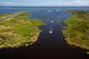 Aerial view of a winding marsh waterway with sailboats and a causeway road, location not identified.