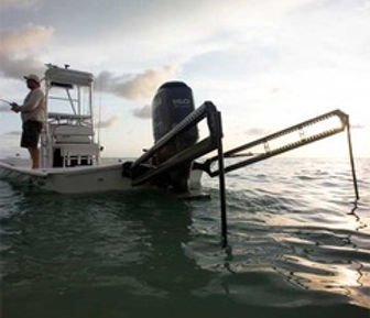 Angler fishing from a flats boat with an outboard motor and raised poling platform in calm shallow water at dusk.