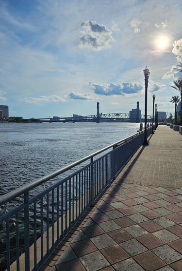 Brick waterfront promenade with metal railing beside a river and a steel drawbridge in the distance, Jacksonville.