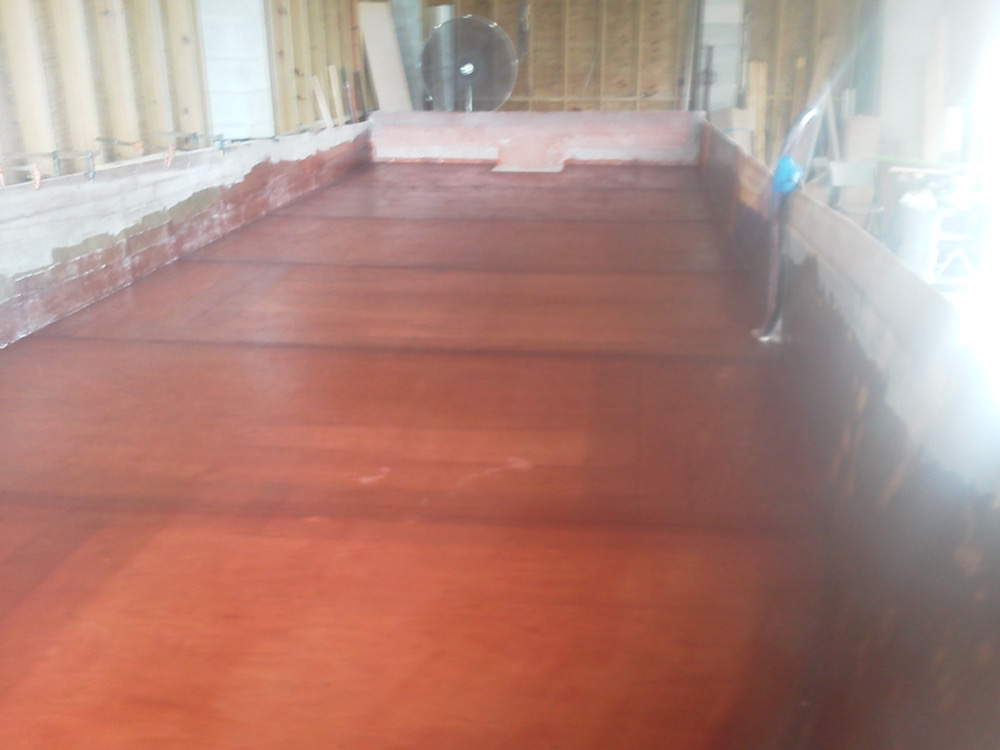 Interior of a wooden boat hull under construction or repair, showing reddish-brown planking and filler along the sides and transom.