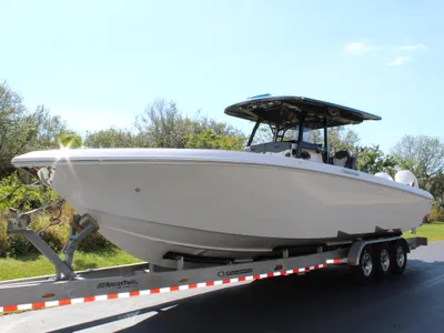 White center console boat with a T-top sitting on a triple-axle trailer on a paved road, with green shrubs and trees behind it.