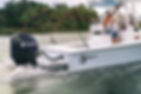Center console boat with a black outboard motor on calm water, with a person standing aboard.