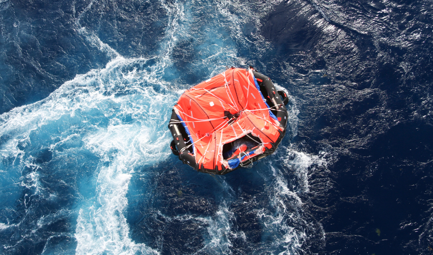 Orange inflatable life raft floating on churning dark blue ocean water with a white wake, viewed from above.