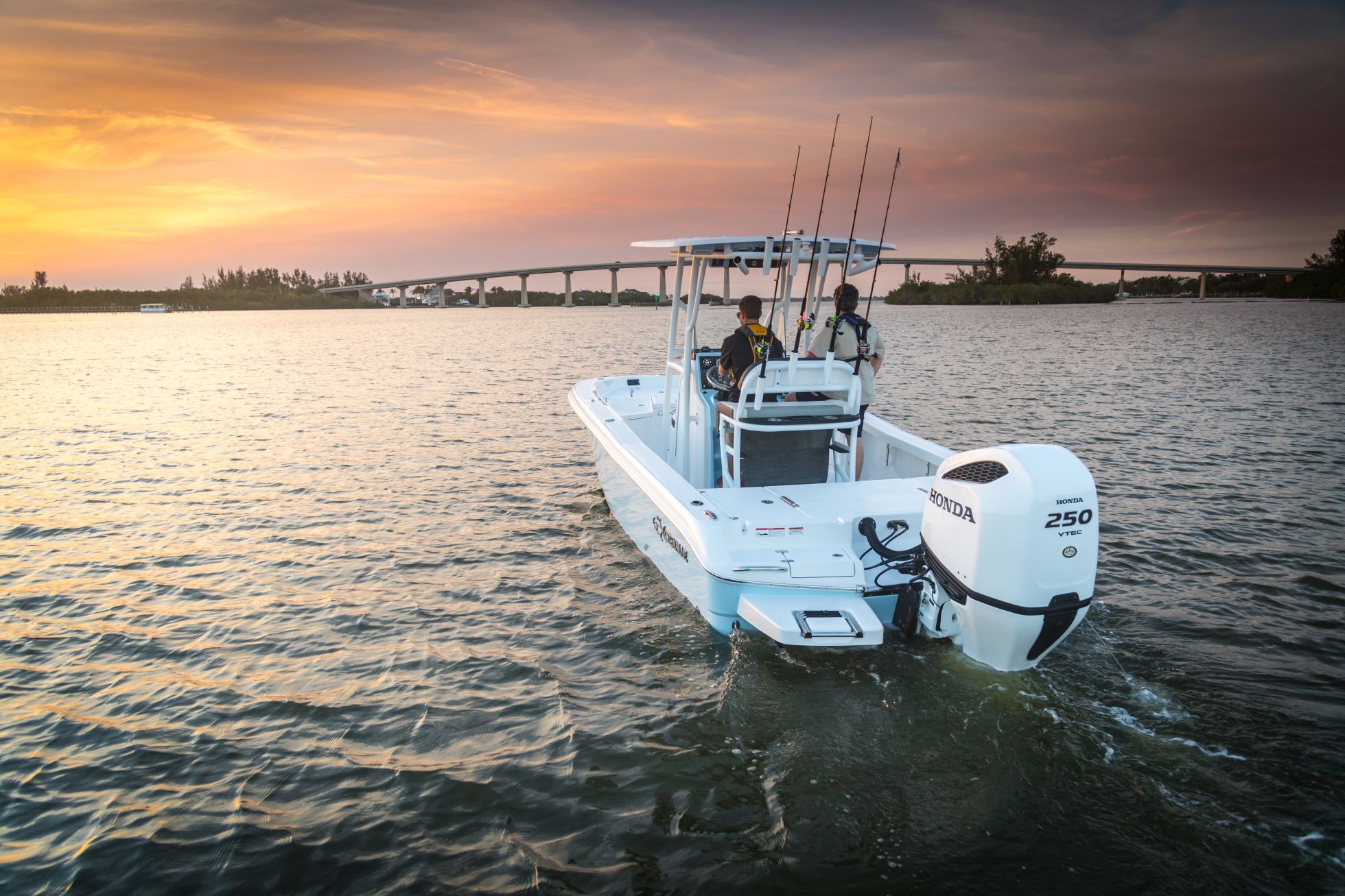 Center console fishing boat with a Honda 250 VTEC outboard cruising a waterway at sunset, with a bridge in the background.