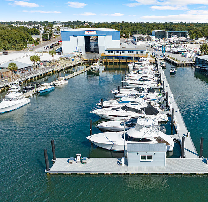 Aerial view of yachts docked at a floating pier beside a large boat repair hangar at Brewer Yacht Yard, Wrightsville Beach.