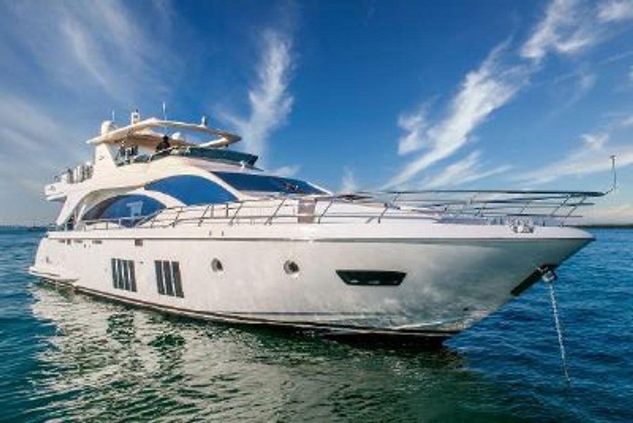 Large white motor yacht with a flybridge and stainless steel railings at anchor on calm blue water.
