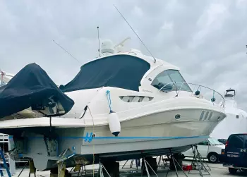 Motor yacht on jack stands with a dark canvas cover over its flybridge in a boatyard.