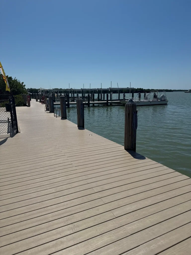 Empty wooden boardwalk dock with mooring pilings and a moored passenger boat at a marina on the water.