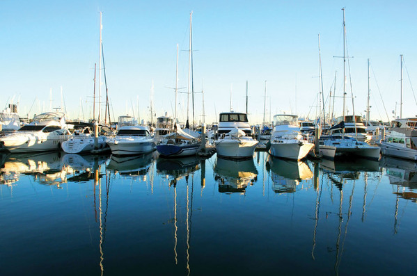 Motor yachts and sailboats moored side by side in a marina with reflections on calm water.