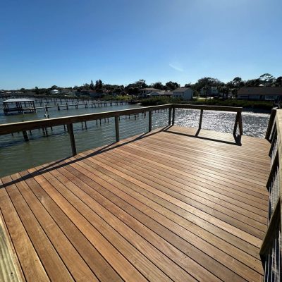 New wooden boardwalk dock with railing overlooking a canal lined with waterfront homes and boat docks.