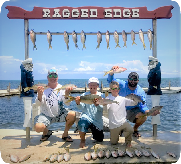 Four anglers posing with their catch on the dock at Ragged Edge, with fish hanging on a rack and open water behind them.