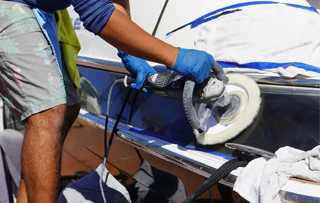 Technician polishing the gelcoat of a white and blue boat with a foam buffing pad, business and town not shown.