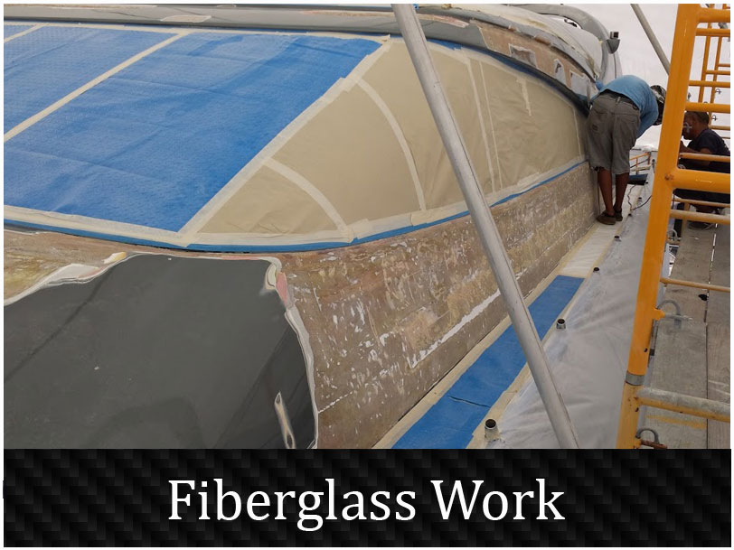 Fiberglass hull repair in progress on a sailboat, with the damaged laminate ground back and workers on scaffolding.