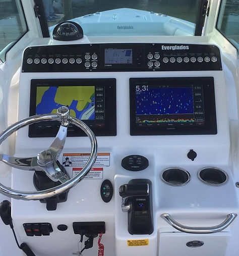 Helm console with twin chartplotter and sonar displays, wheel and engine controls on an Everglades boat.