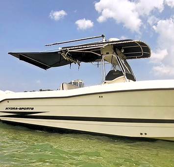 White Hydra-Sports center console boat with a black canvas bimini and T-top cruising on green water.