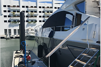 White motor yacht docked at a marina with a tall residential building behind it.
