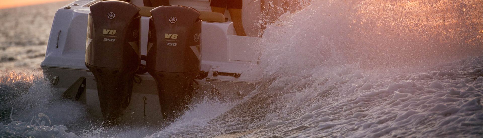 Twin Yamaha V8 350 outboard motors powering a boat through churning white spray at sunset.