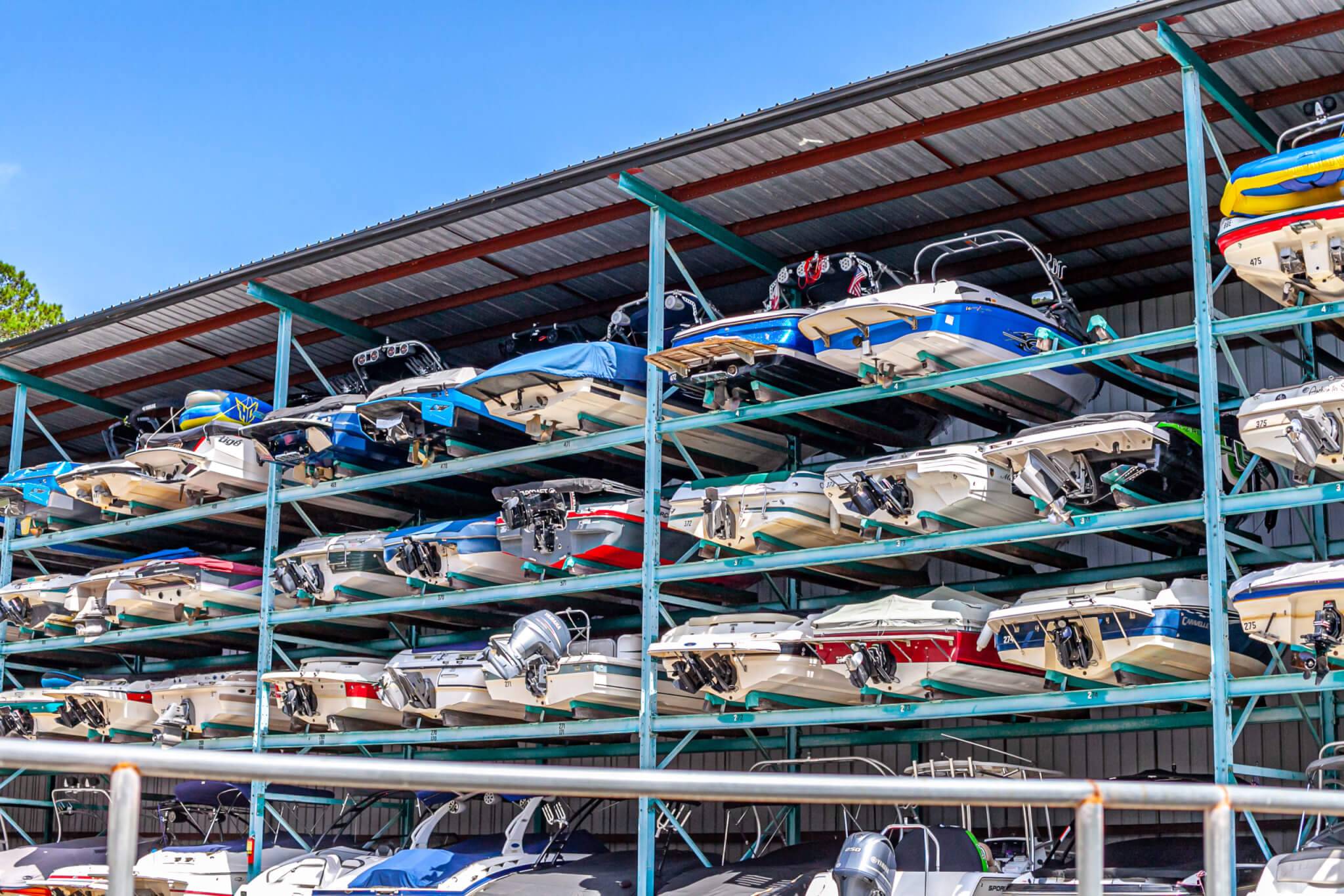 Boats stored on multi-tier teal metal racks under a covered metal roof at a boat storage facility.