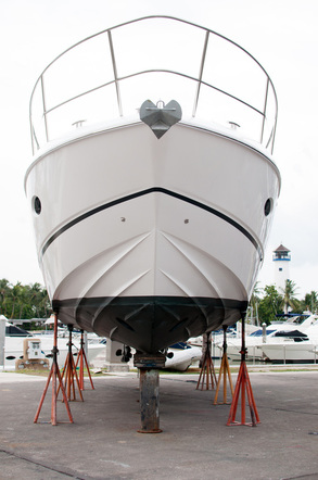 White motor yacht on orange jack stands in a boatyard, with other boats and palm trees behind it.