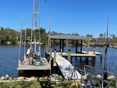 Dock and boat lift installation with a person working on a floating dock over a waterway, with trees along the shoreline.