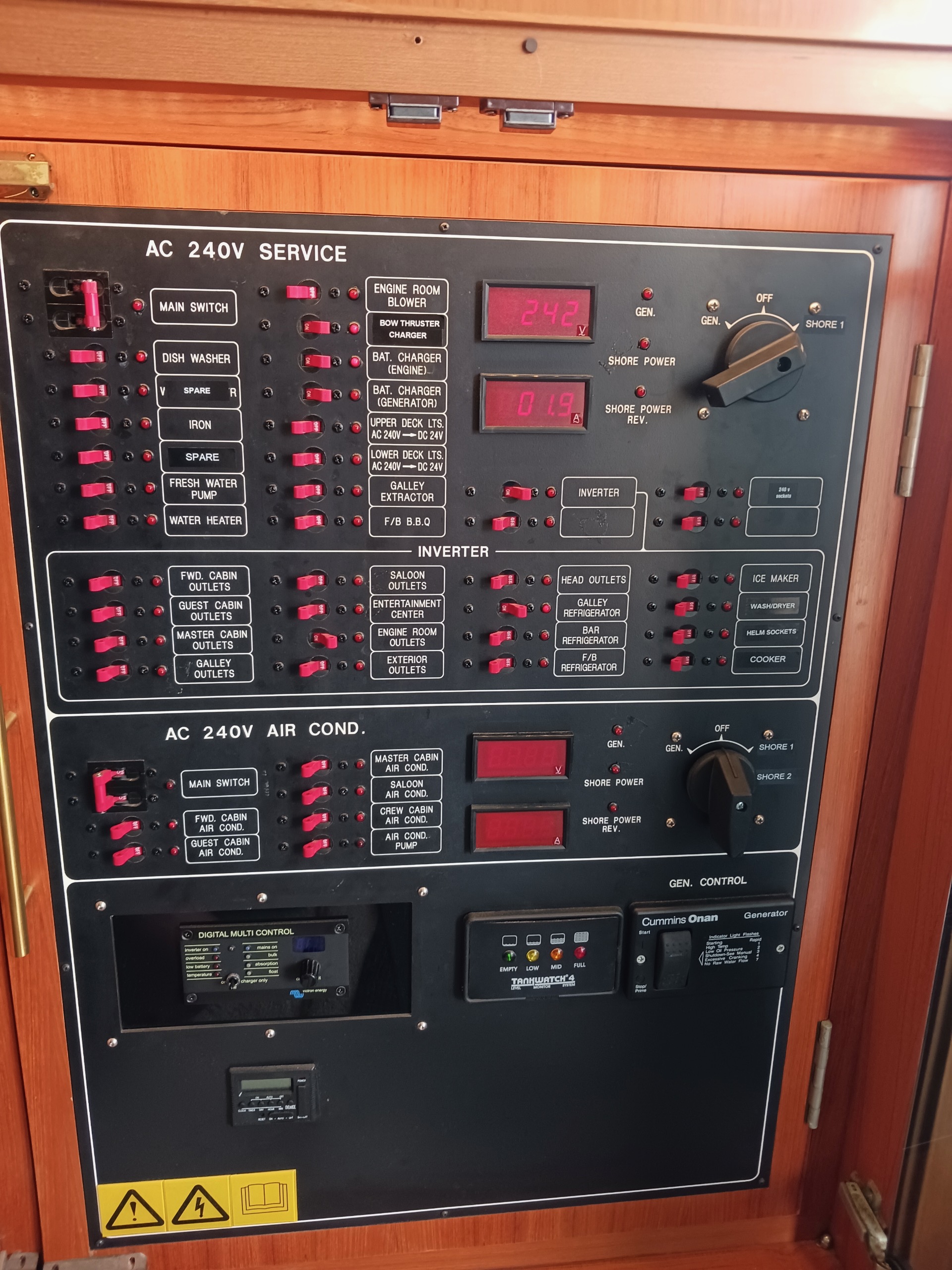 AC 240V electrical distribution panel with breaker switches, digital meters, inverter circuits, and Cummins Onan generator controls aboard a yacht.