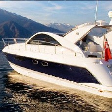 Motor yacht on calm lake water with mountains in the background.