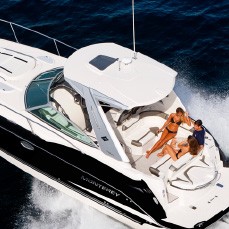 Black-and-white motor yacht with two people on its foredeck cruising across open blue water.