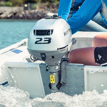 Honda 2.3 outboard motor mounted on a small tender boat with a person steering through splashing water.