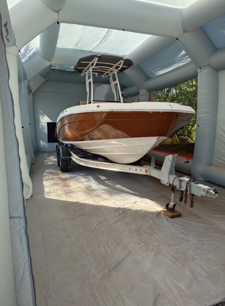 Center console boat with a brown and white hull sitting on a trailer inside an inflatable paint booth enclosure.