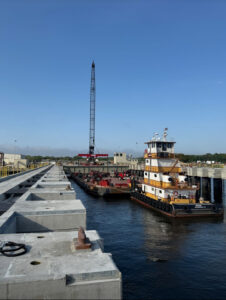 Yellow and white towboat moored in a lock chamber beside concrete lock walls, with a crane in the background.