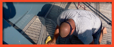 A worker kneeling on a teak boat deck doing maintenance work near the helm.